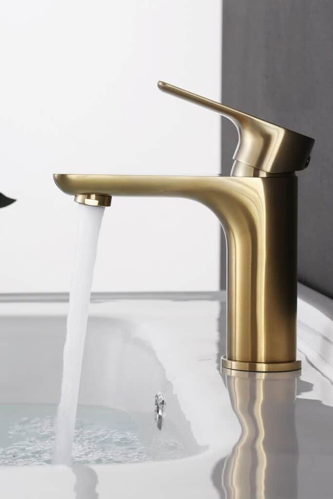 Modern brass faucet pouring water into white sink in minimalist bathroom setting.