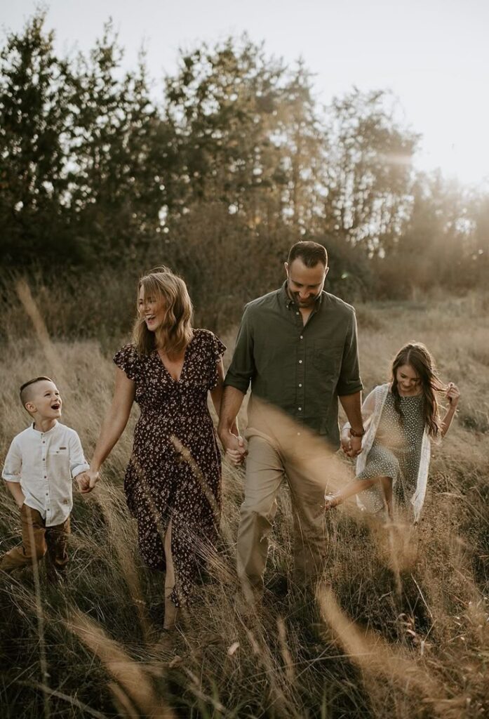 Family walking through a grassy field at sunset, enjoying a joyful moment together in nature.
