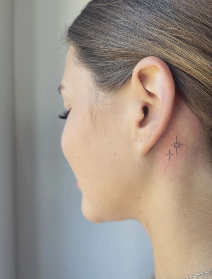 Minimalist star tattoo behind ear on woman's neck, close-up. Small, delicate ink design.
