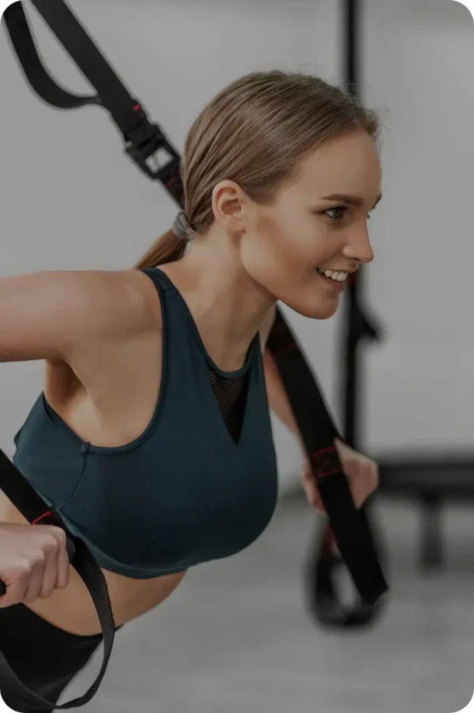 Woman performing TRX workout, smiling and focused in gym setting.