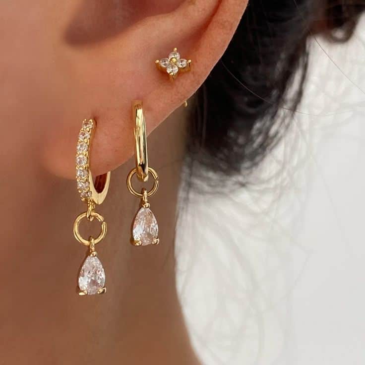 Elegant gold hoop earrings with dangling teardrop stones and a small diamond stud on ear.