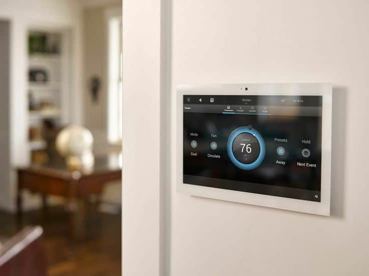 Smart thermostat on a wall displaying 76°F in a modern home interior, optimizing energy efficiency and climate control.