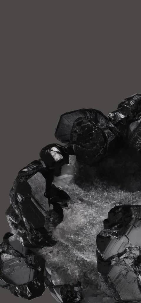 Close-up of shiny black crystals against dark background, highlighting their geometric shapes and glossy texture.