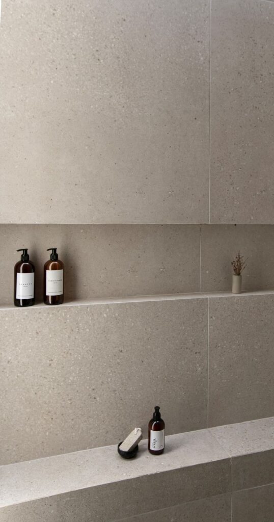 Minimalist bathroom shelf with stone decor, two brown bottles, and a pumice stone in a bowl.