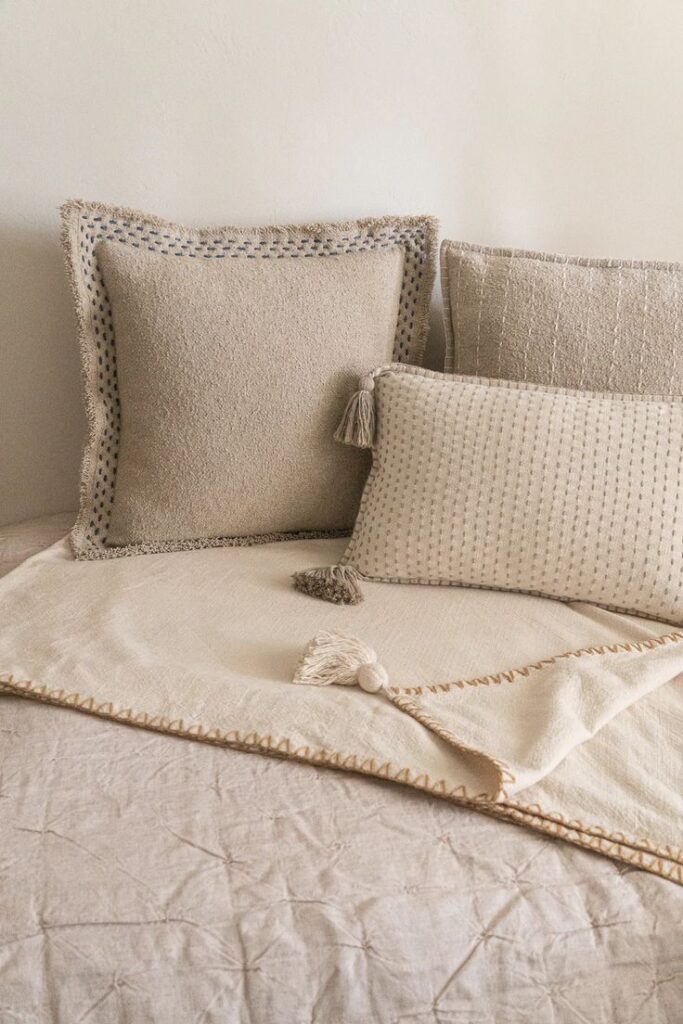 Cozy beige throw pillows on a bed with a textured blanket for a warm, minimalist home decor style.