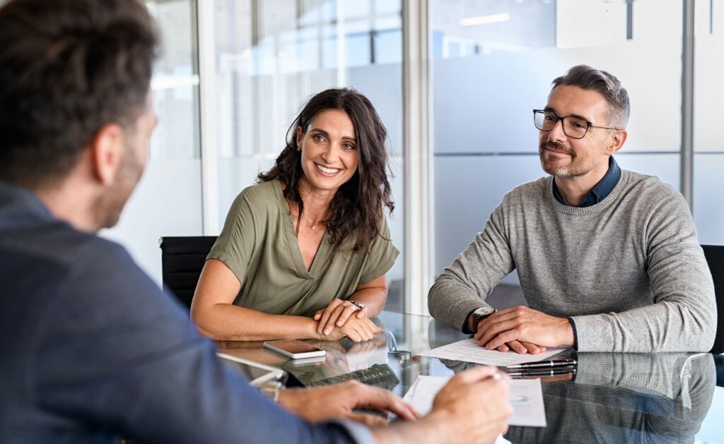 Business meeting with a smiling woman and two men discussing paperwork at a glass table in a modern office setting.