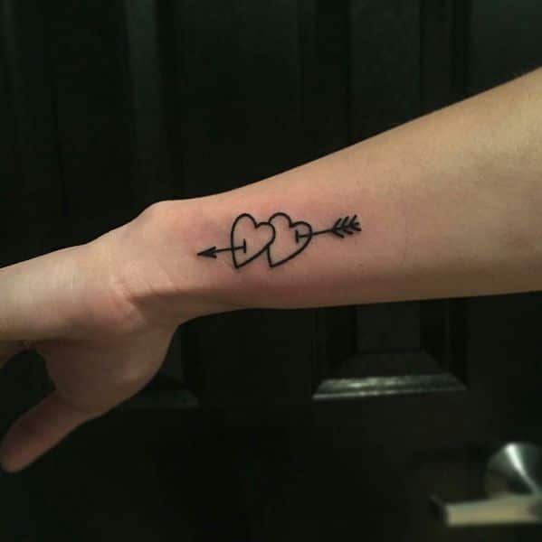 Minimal heart tattoo with arrow on forearm, symbolizing love and connection.