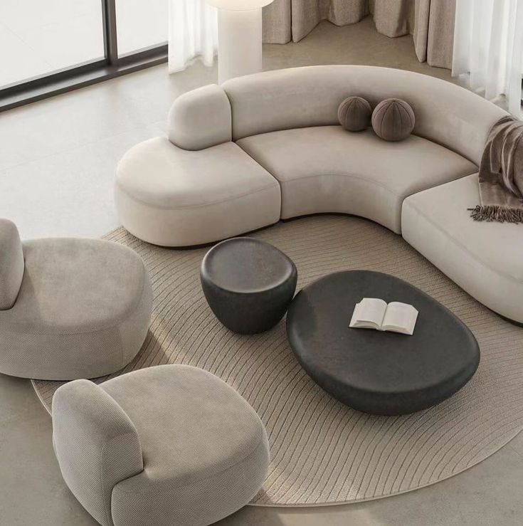 Modern beige sectional sofa with round coffee tables on textured rug in bright living room.