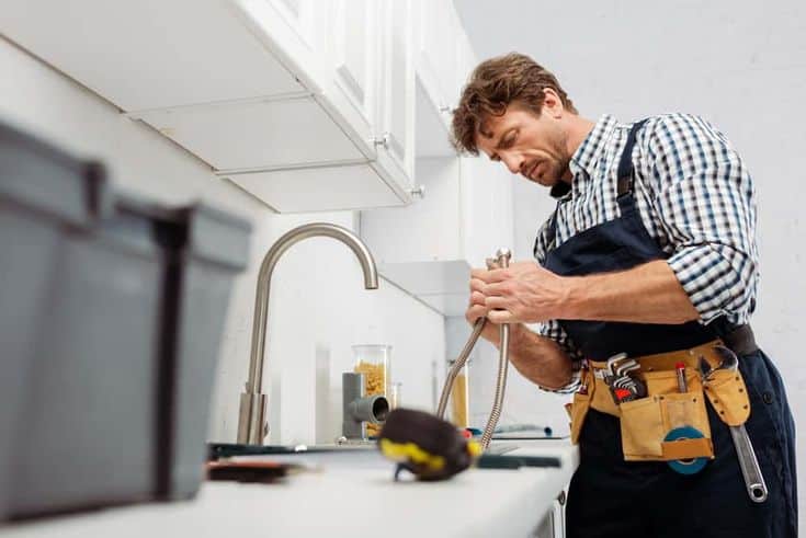 Handyman fixing kitchen sink with tools in apron.