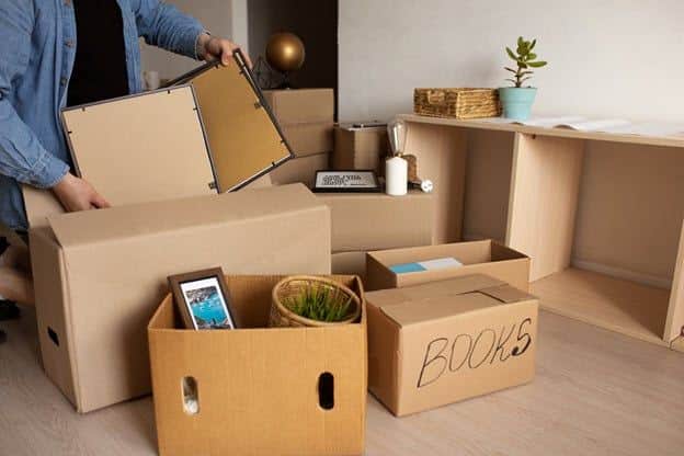 Person organizing items into labeled boxes during a home move, including a box of books and various household items.
