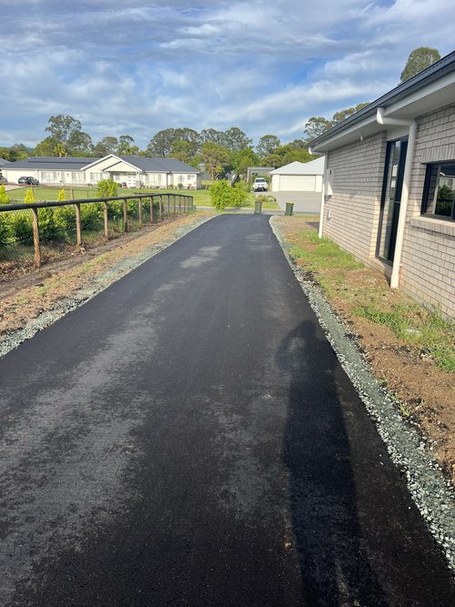 Freshly paved driveway beside a modern house, leading towards a sunny suburban neighborhood.