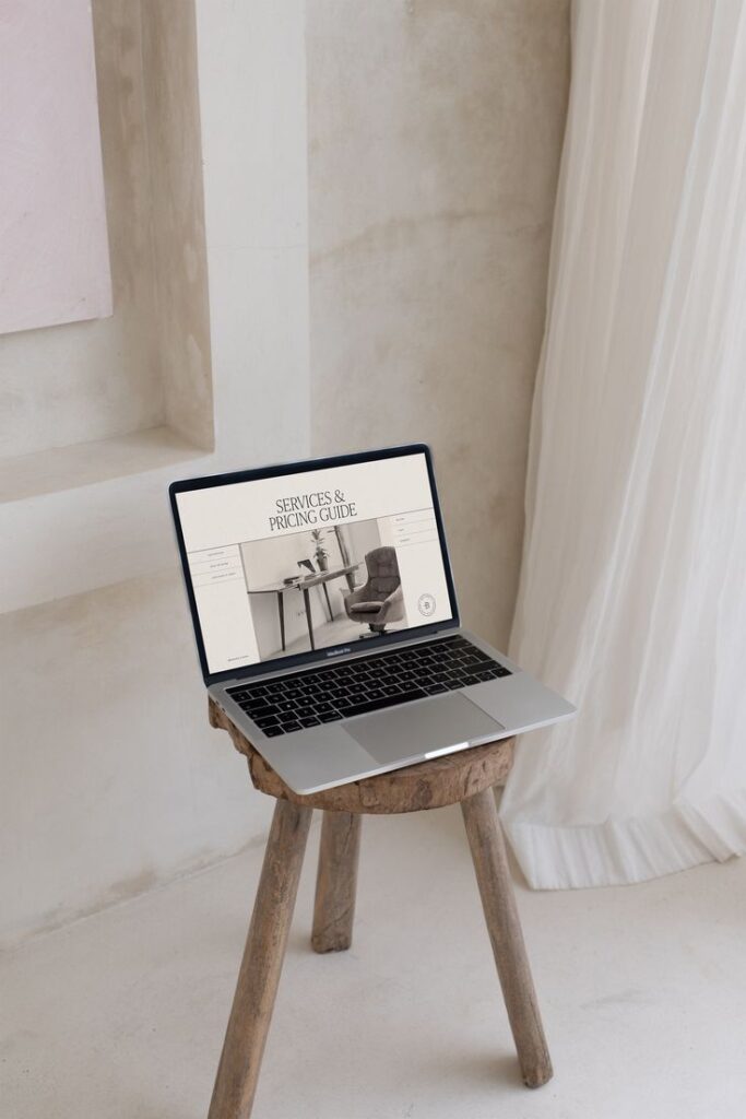 Laptop on rustic stool with Services & Pricing Guide displayed, set in a minimalist room with white curtains.