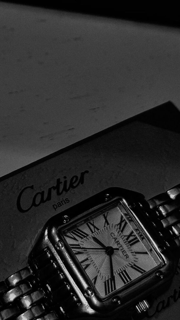 Luxury Cartier watch with Roman numerals and metallic band on branded packaging.