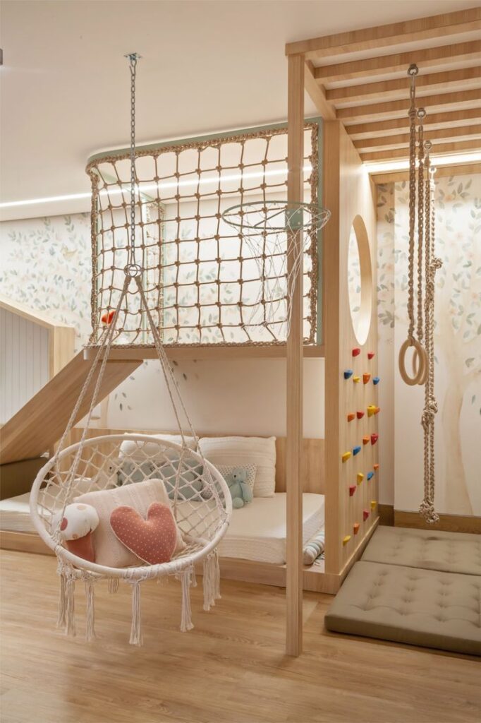 Children's indoor playroom with climbing wall, rope swings, and cozy seating area with pillows.