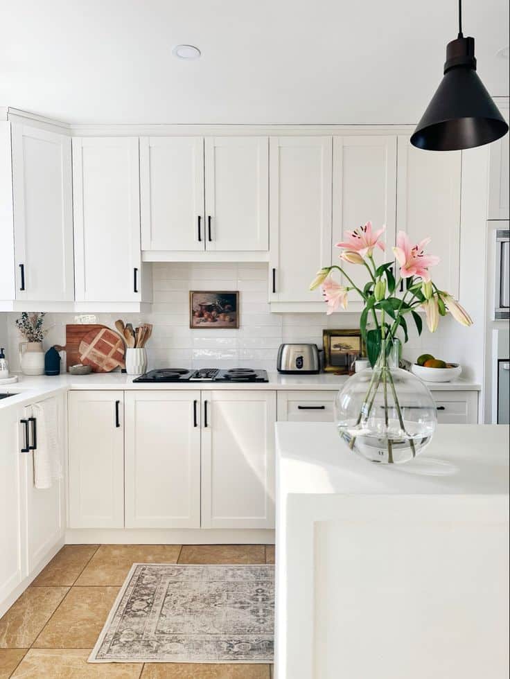 Modern kitchen with white cabinets, black handles, and pink lilies in a glass vase on the island.