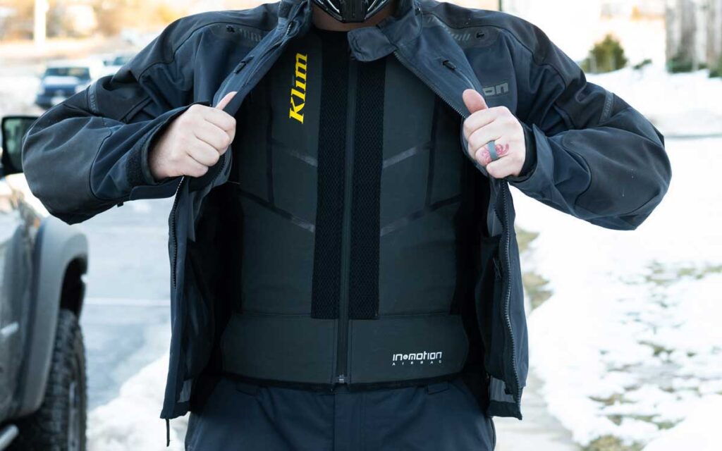 Person wearing motorcycle jacket showing protective vest outdoors.