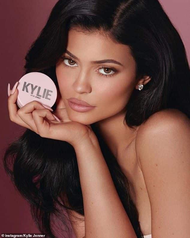 I don't know who this person is, but here's a possible alt text:Person holding pink cosmetic compact, long dark hair, glamorous makeup look.