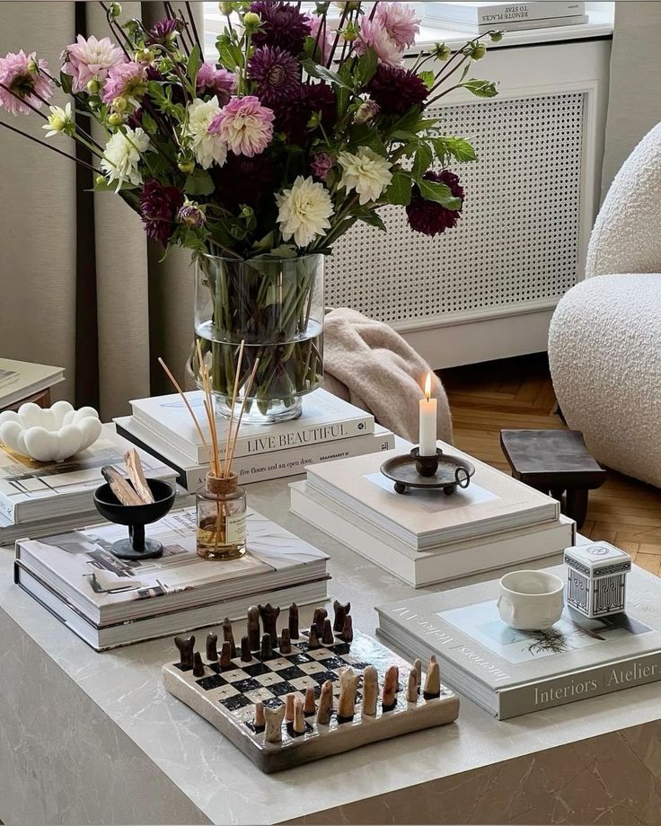 Cozy living room with flowers, candles, and books on a coffee table featuring a unique chess set.