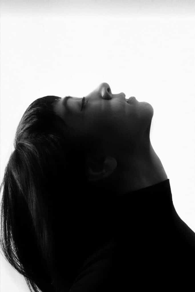 Silhouette of person with head tilted back, eyes closed, in a black and white photo against a bright background.