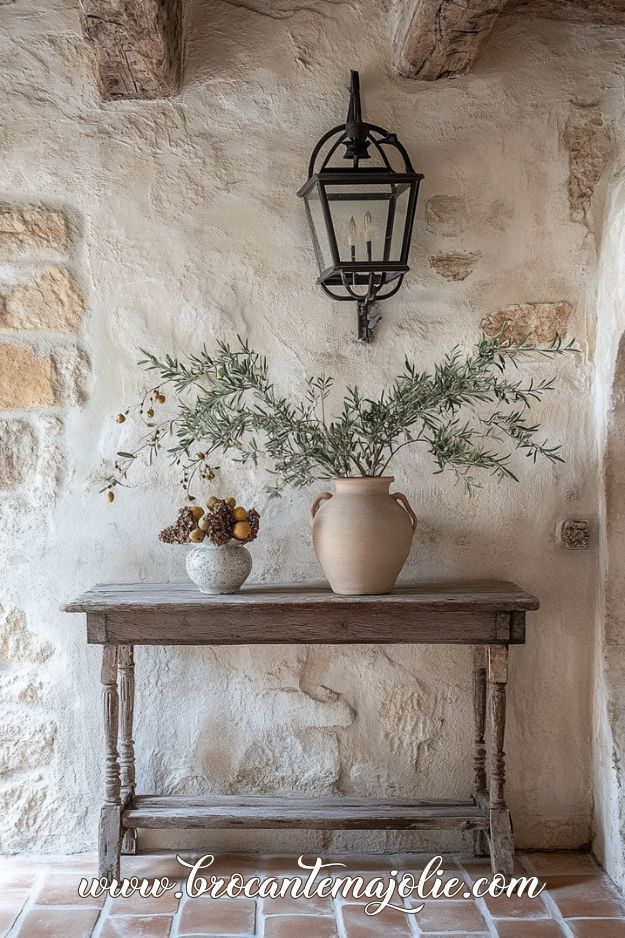 Rustic wooden table with vases and plants under a vintage wall lantern on a textured stone wall.