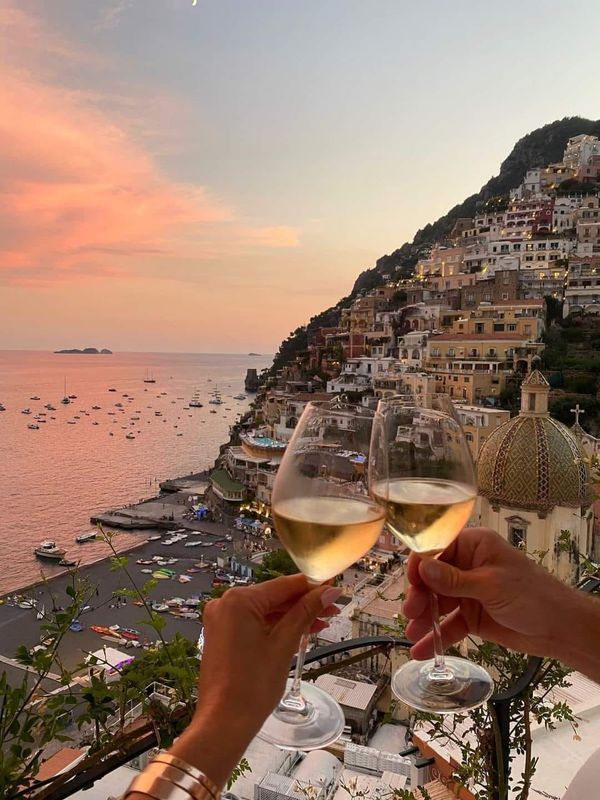 Toasting with wine glasses overlooking a scenic coastal view in Positano at sunset.