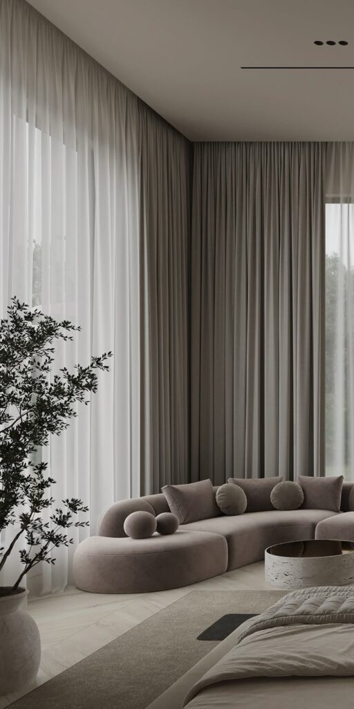 Modern living room with a curved beige sofa, floor-to-ceiling curtains, large plant, and a round coffee table.