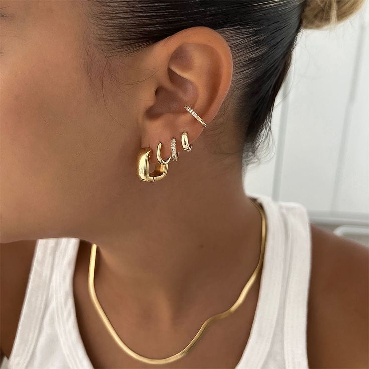 Woman wearing multiple gold earrings and necklace with a sleek white top.