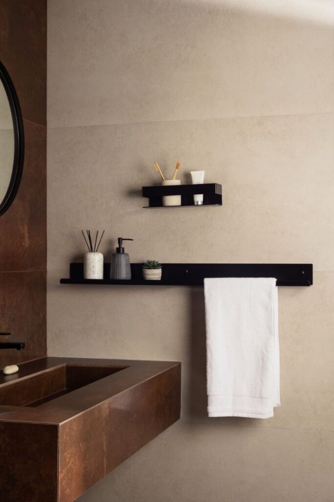 Minimalist bathroom with brown sink, shelf storage, and white towel on black rail. Modern decor with neutral tones.