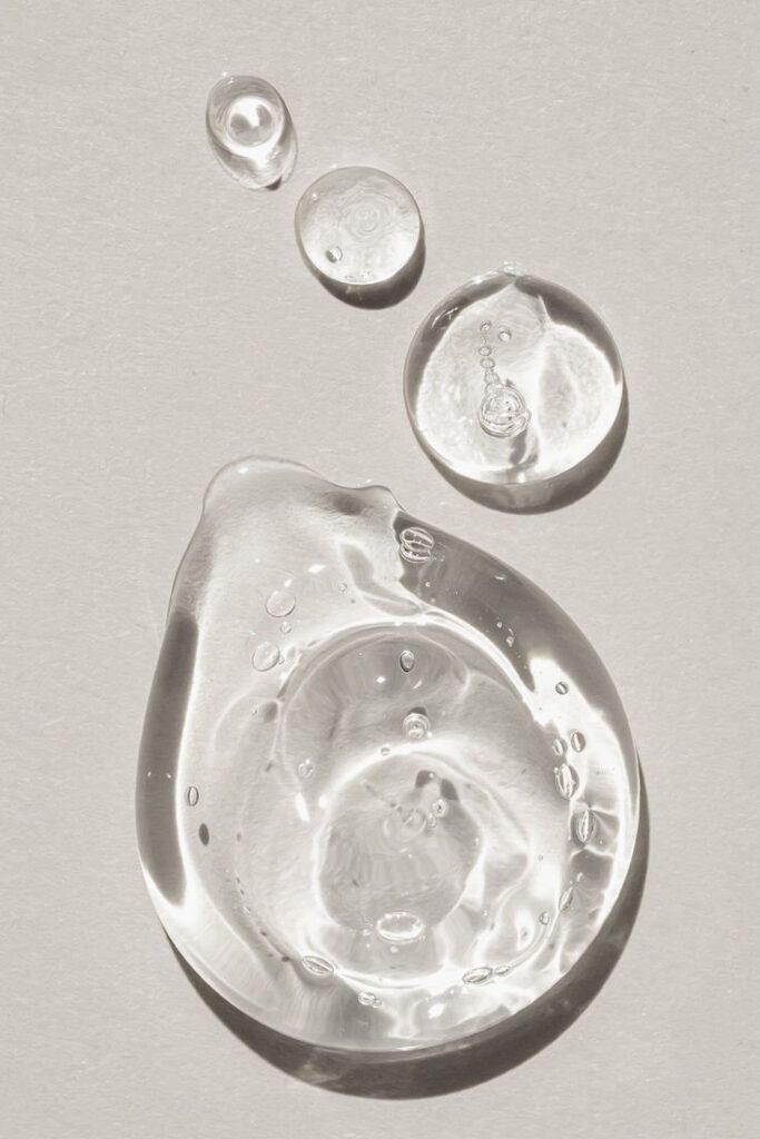 Clear serum droplets on beige background, showcasing a skincare product texture and light reflection.
