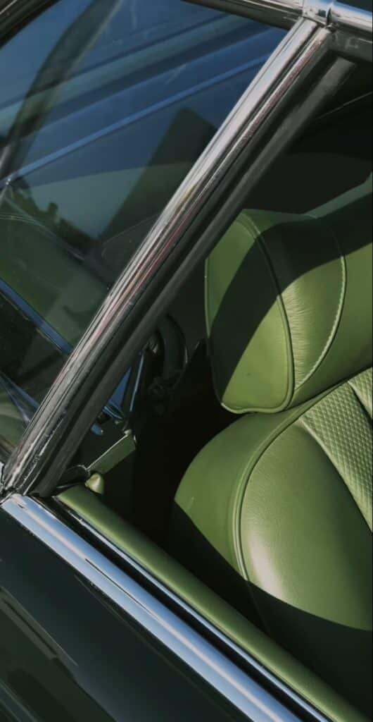 Green leather car seat through open window with chrome trim in sunlight.