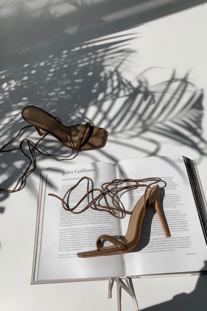 Strappy high heels on a book with floral shadows. Fashion and style concept.