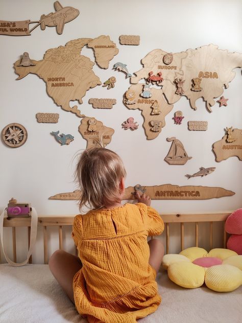 Child in yellow dress explores wooden world map on wall in cozy room.
