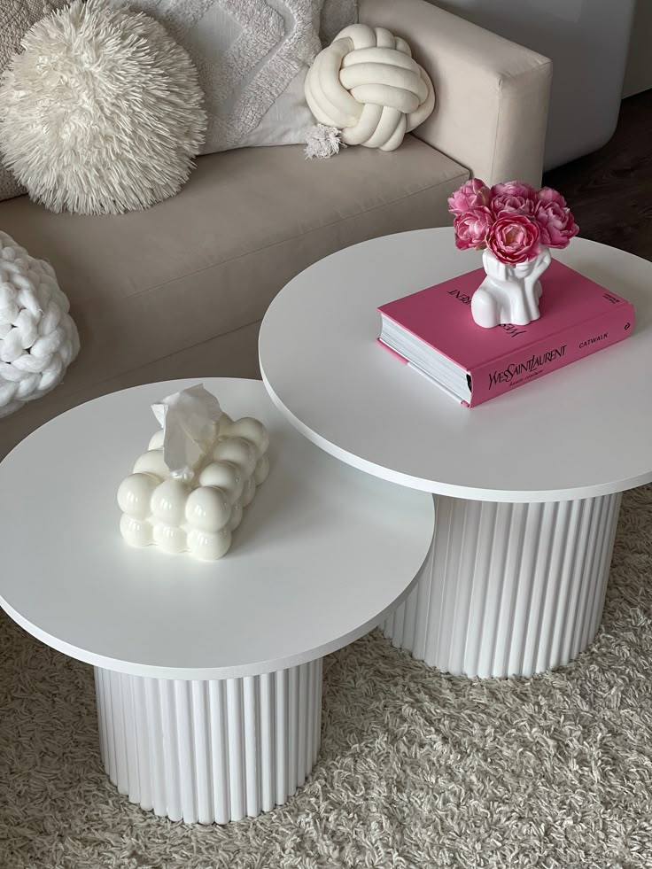 Modern white coffee tables with decorative candles, a pink book, and floral arrangement in stylish living room.