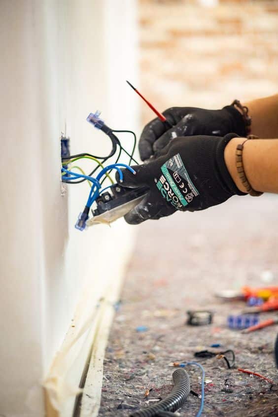 Electrician wearing gloves works on wiring and electrical outlet installation in a wall.