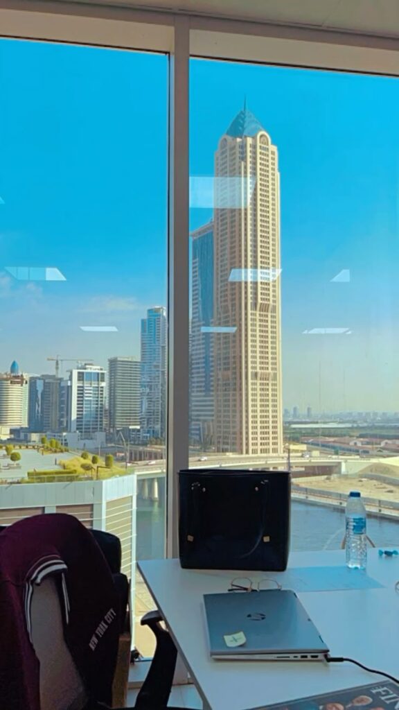 Office Space in Dubai 1 Office with laptop, water bottle, and stunning city skyline view through large window. | Sky Rye Design Office with laptop, water bottle, and stunning city skyline view through large window.