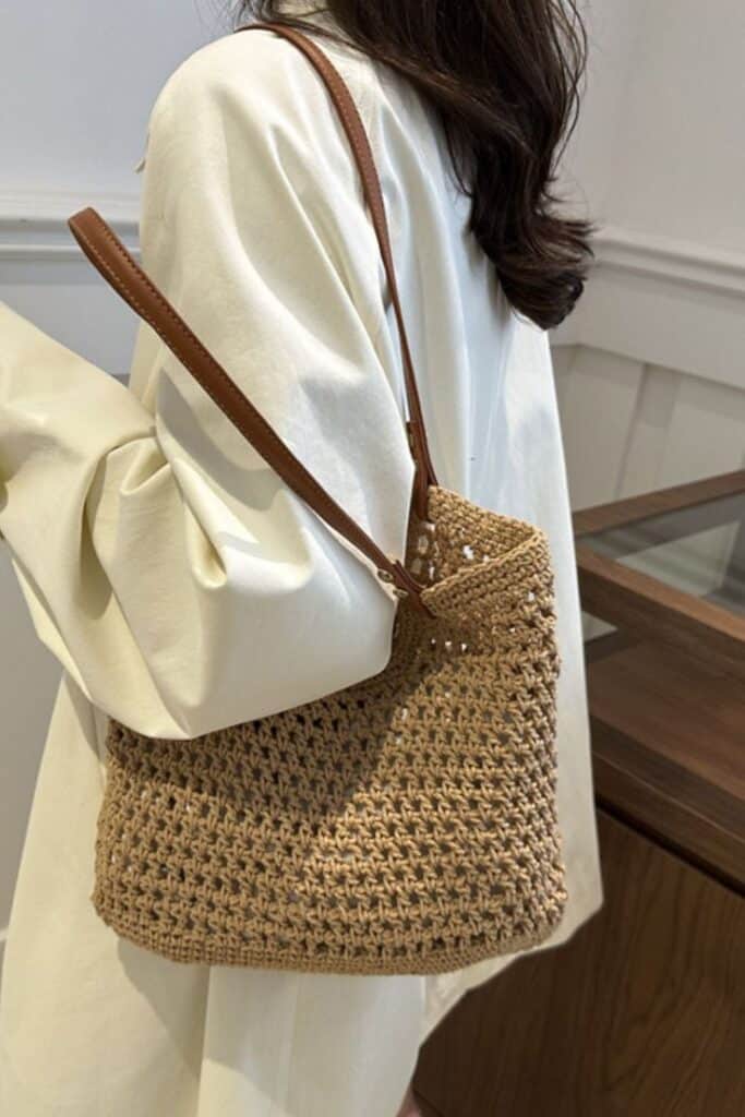 Woman in white coat carrying a stylish woven straw handbag with leather strap.
