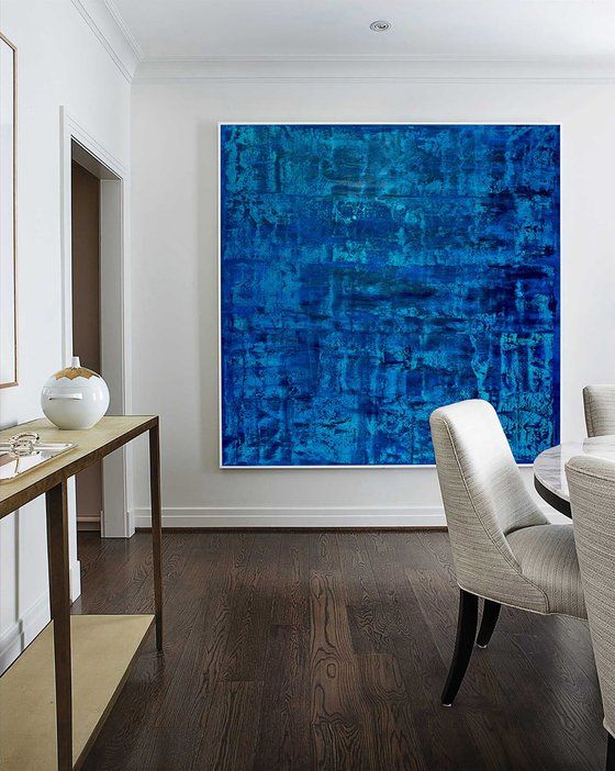 Modern dining room featuring large abstract blue painting on the wall, with wood flooring and elegant chairs.