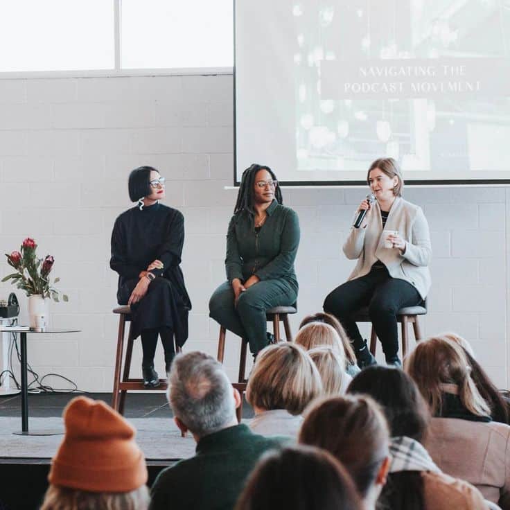 Three women speaking on a panel about podcasting at a conference, engaging an attentive audience.