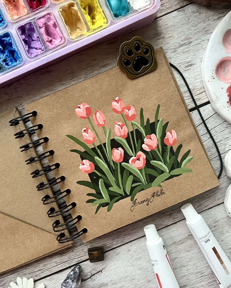 Painted tulips today 🌷✨ Tried out a new kraft Illustrated pink tulips in a sketchbook with watercolor paints and art supplies nearby. | Sky Rye Design Illustrated pink tulips in a sketchbook with watercolor paints and art supplies nearby.