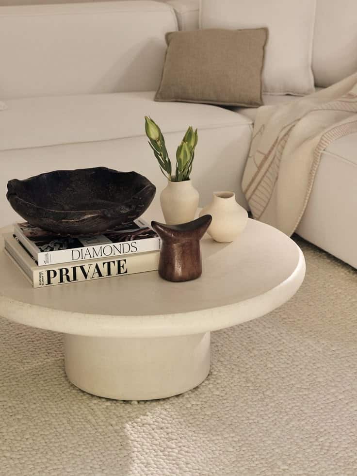 Modern coffee table with books, vases, and decor on a cozy white rug in a minimalist living room setting.