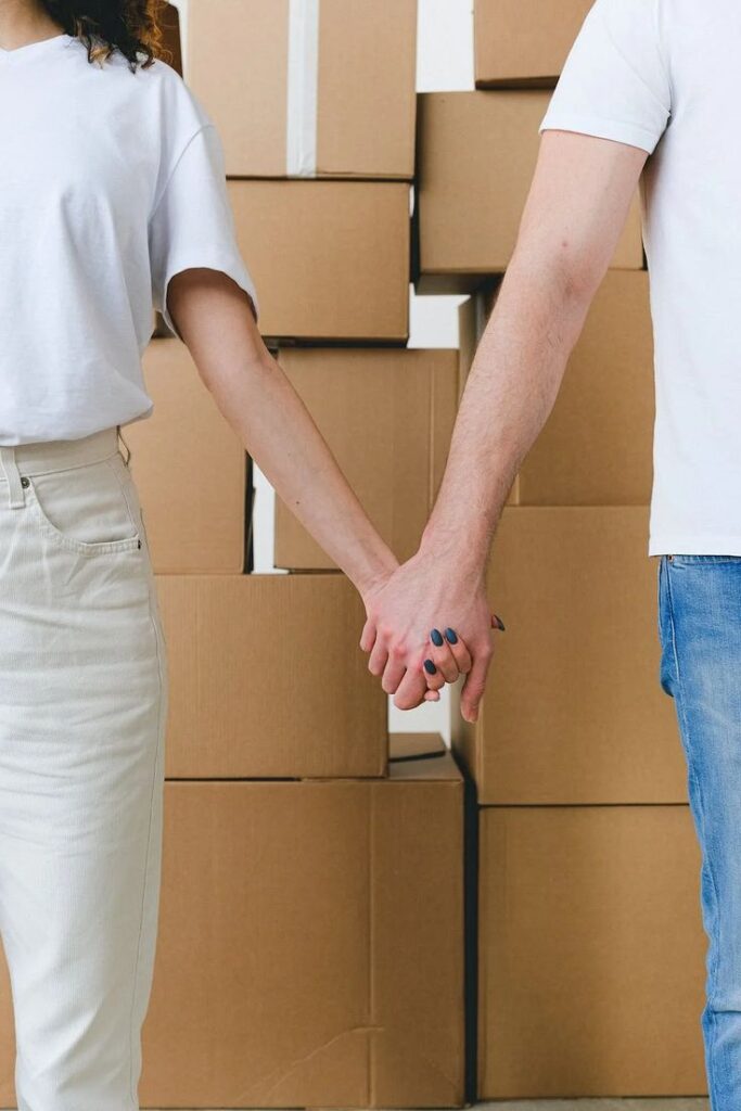 Couple holding hands in front of moving boxes, symbolizing moving or new beginnings.