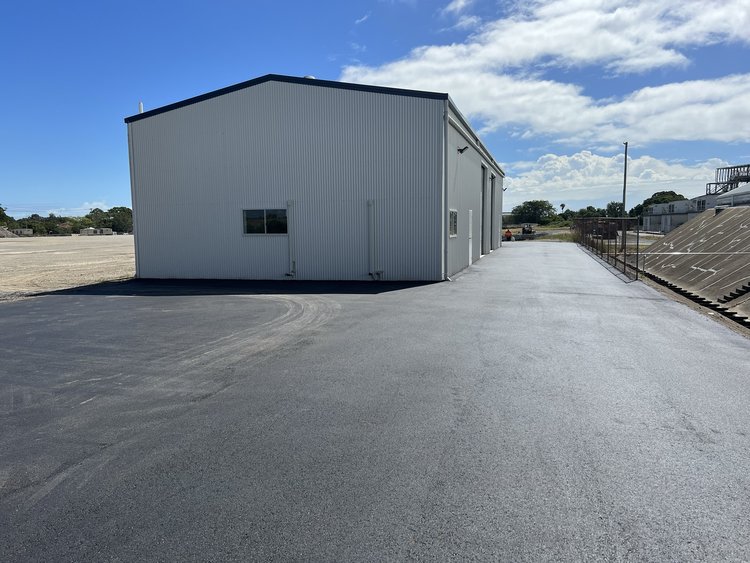 Industrial building with paved asphalt driveway under a clear blue sky.