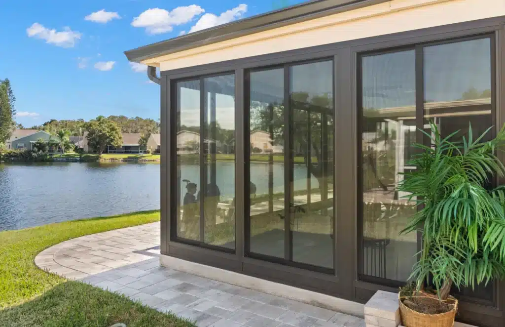 Modern sunroom with large glass windows overlooking a tranquil lake and lush greenery.