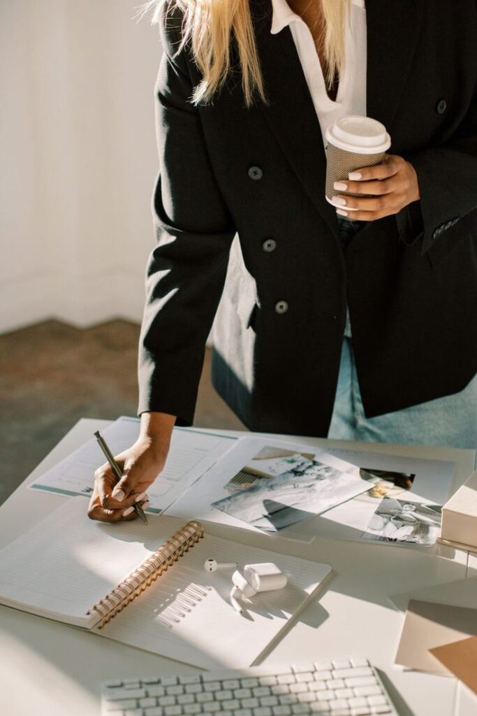 Businesswoman planning with notebook and coffee, focus on desk with documents and accessories.