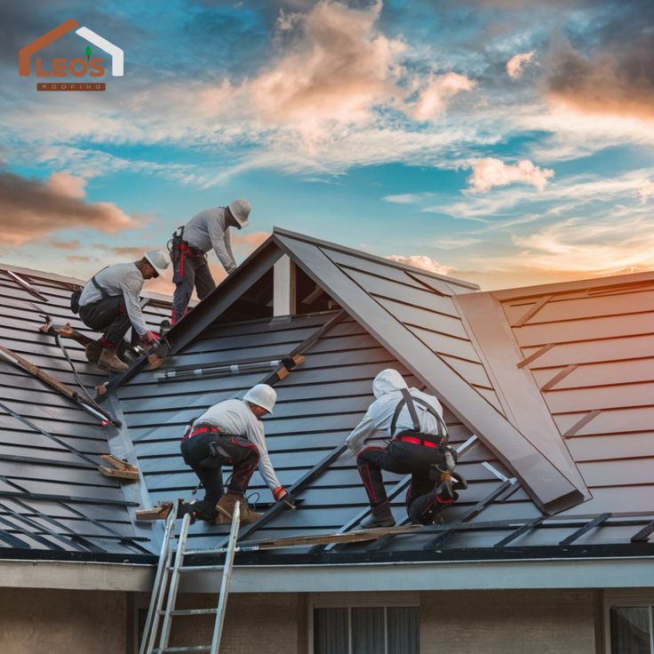 Roofers installing metal panels on a residential roof at sunset.