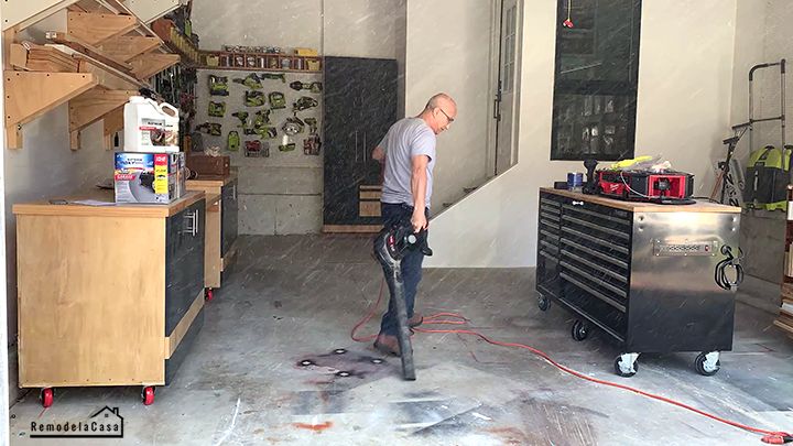 Person vacuuming a well-organized workshop with tools, cabinets, and shelves for garage cleanliness.