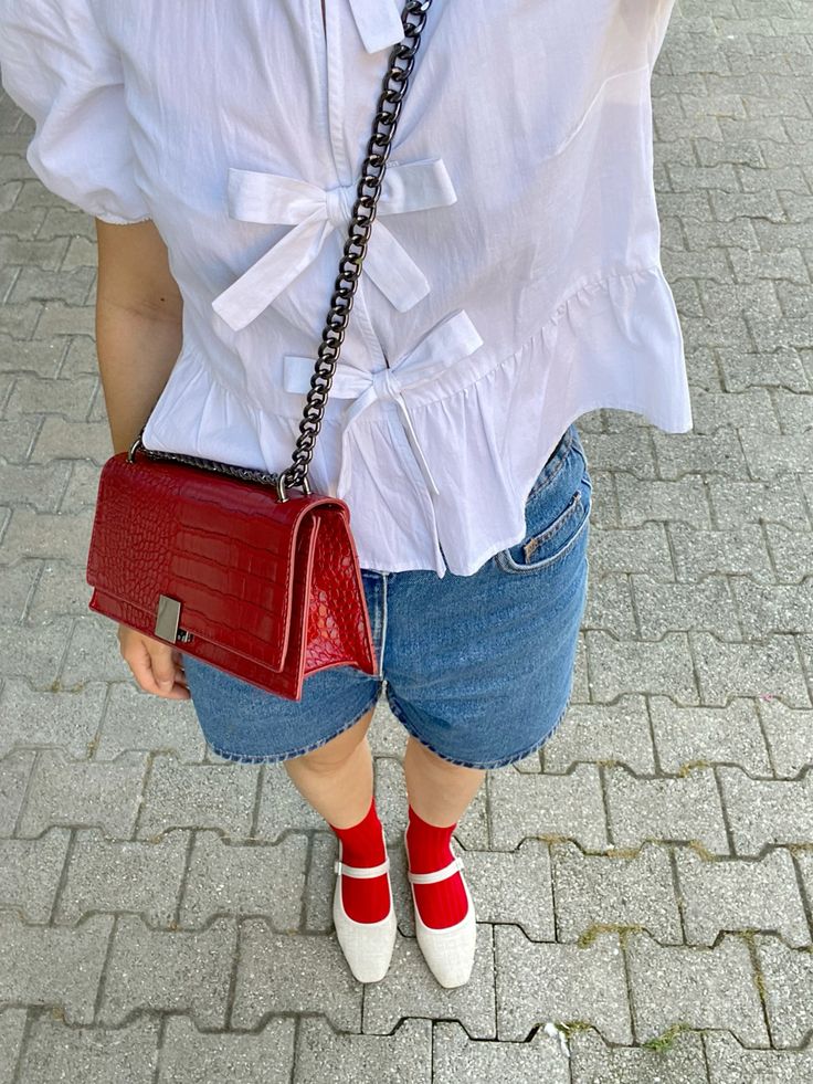 Red bag ans socks euro summer outfit Woman in white blouse and denim shorts with red handbag and red socks with white shoes on pavement. Fashionable summer look. | Sky Rye Design Woman in white blouse and denim shorts with red handbag and red socks with white shoes on pavement. Fashionable summer look.