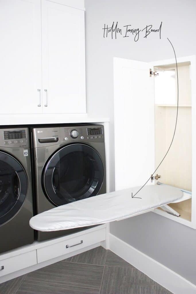 Laundry room with built-in ironing board folded out, next to washer and dryer under white cabinets.
