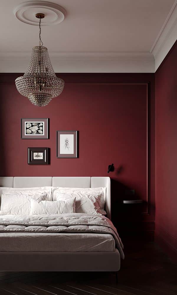 Elegant bedroom with burgundy walls, crystal chandelier, art frames, and a plush white bed for a luxurious ambiance.