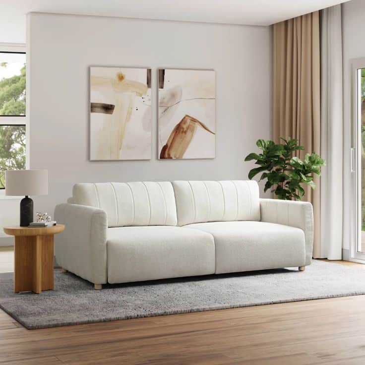 Modern living room with cream sofa, abstract wall art, gray rug, and indoor plant near a sunlit window.
